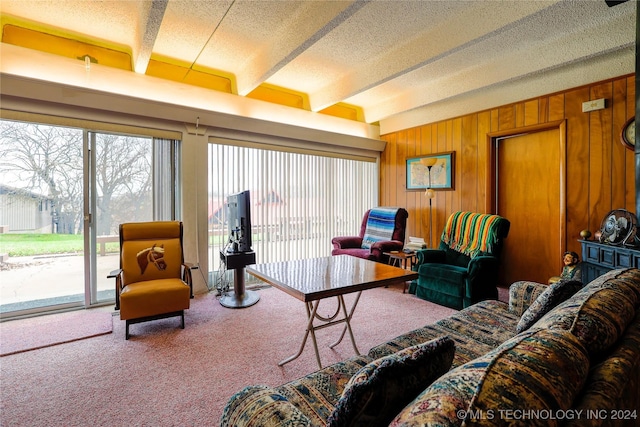 living room with beamed ceiling, a textured ceiling, carpet flooring, and wooden walls