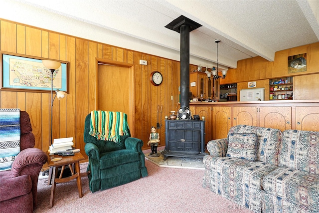 carpeted living room featuring beamed ceiling, a wood stove, wooden walls, and a chandelier