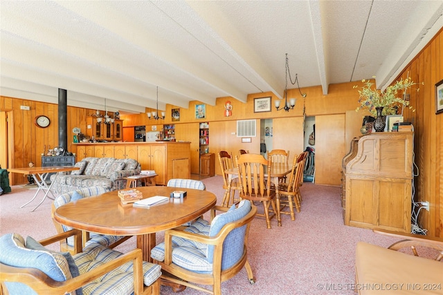 dining space with beam ceiling, a wood stove, wooden walls, and light carpet