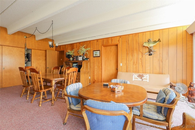 dining room with a chandelier, beam ceiling, carpet flooring, and wood walls