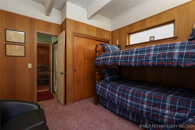 bedroom featuring wooden walls, a closet, carpet floors, and a textured ceiling