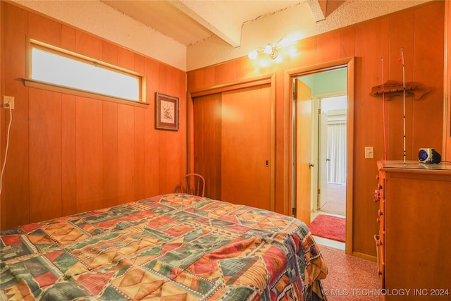 carpeted bedroom featuring beam ceiling, wooden walls, and a closet