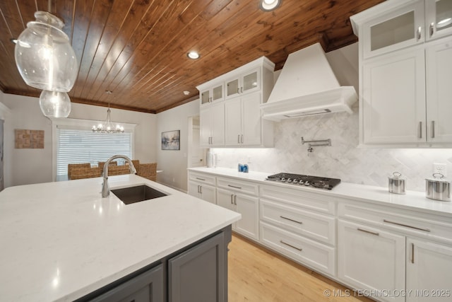 kitchen featuring a sink, white cabinetry, custom exhaust hood, glass insert cabinets, and stainless steel gas stovetop