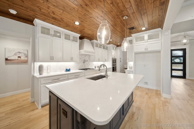 kitchen featuring glass insert cabinets, a sink, and a kitchen island with sink