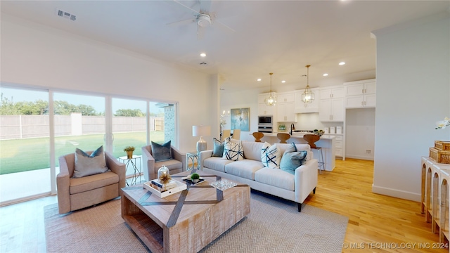 living room featuring ceiling fan, sink, and light wood-type flooring