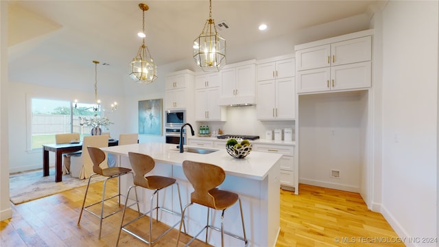 kitchen featuring white cabinetry, sink, stainless steel appliances, decorative light fixtures, and a kitchen island with sink