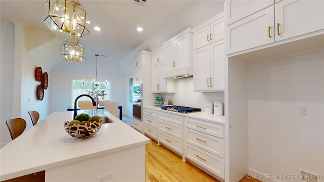 kitchen with white cabinets, decorative light fixtures, sink, and an island with sink