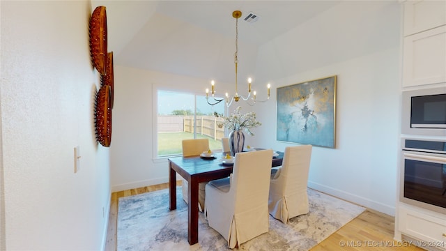 dining room with light hardwood / wood-style floors, lofted ceiling, and an inviting chandelier