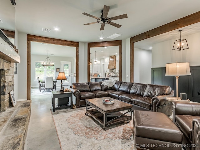 living room with beam ceiling, a fireplace, concrete floors, and ceiling fan with notable chandelier