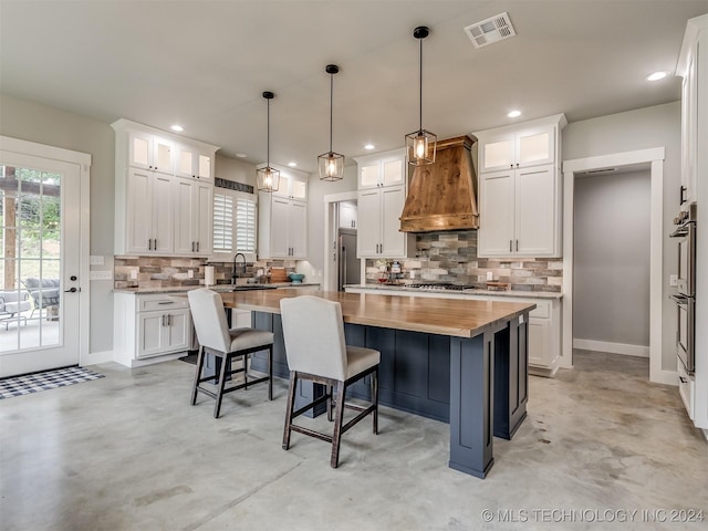 kitchen featuring white cabinets, custom range hood, a kitchen island, and hanging light fixtures