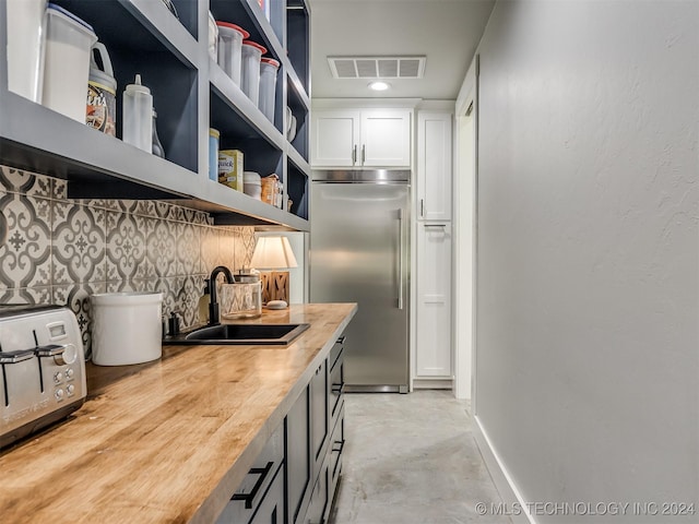 kitchen with butcher block counters, sink, decorative backsplash, stainless steel built in fridge, and white cabinets