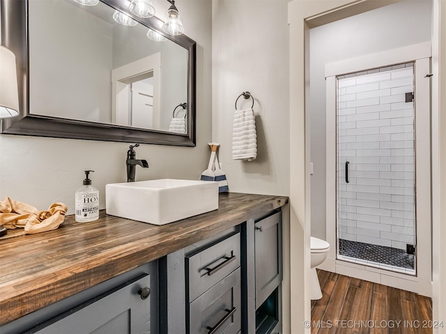 bathroom with a shower with door, vanity, wood-type flooring, and toilet