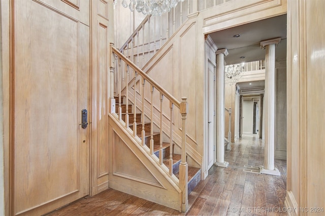 stairway with hardwood / wood-style floors, an inviting chandelier, and ornate columns