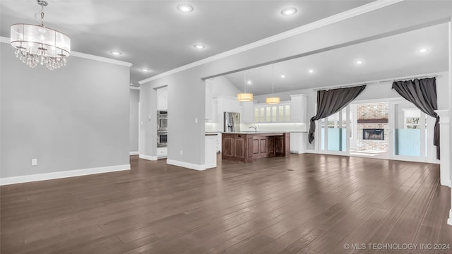 unfurnished living room with a fireplace, crown molding, sink, a chandelier, and dark hardwood / wood-style floors