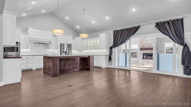 kitchen with decorative backsplash, appliances with stainless steel finishes, a kitchen island with sink, a fireplace, and white cabinetry