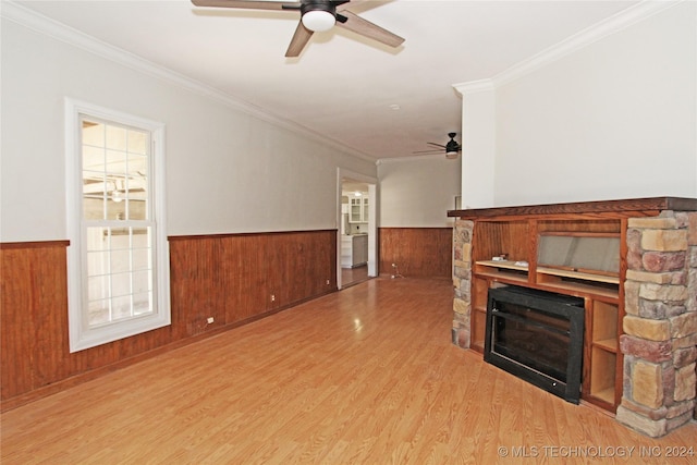 unfurnished living room with ceiling fan, a stone fireplace, light wood-type flooring, and ornamental molding