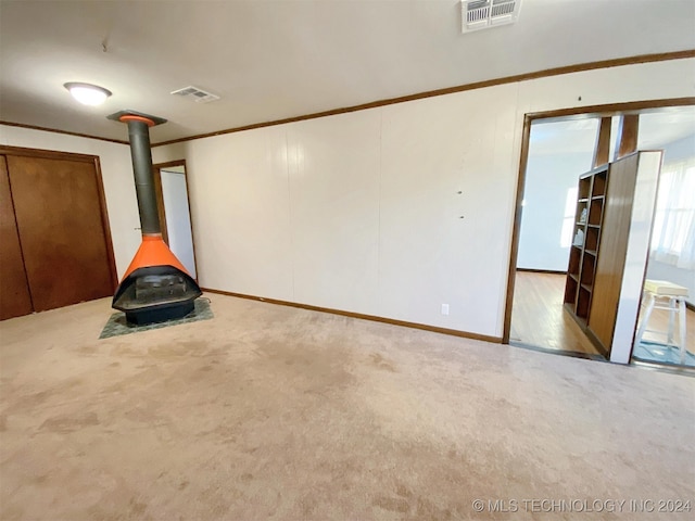 empty room with a wood stove, light carpet, and crown molding