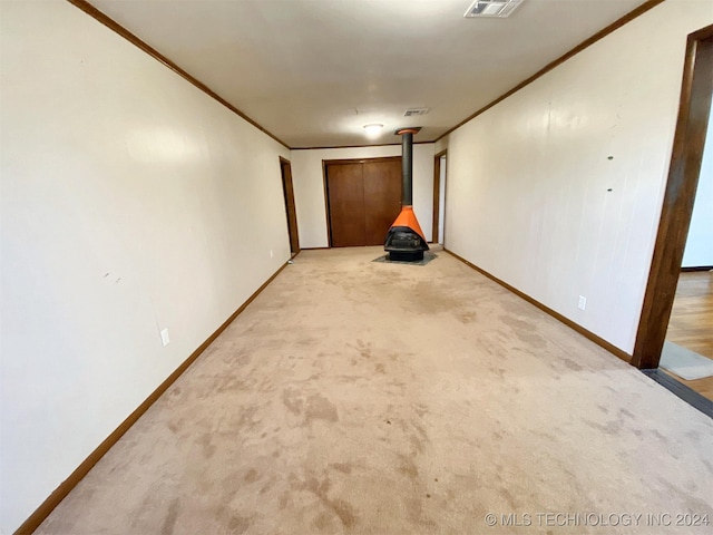 spare room with a wood stove, crown molding, and light colored carpet