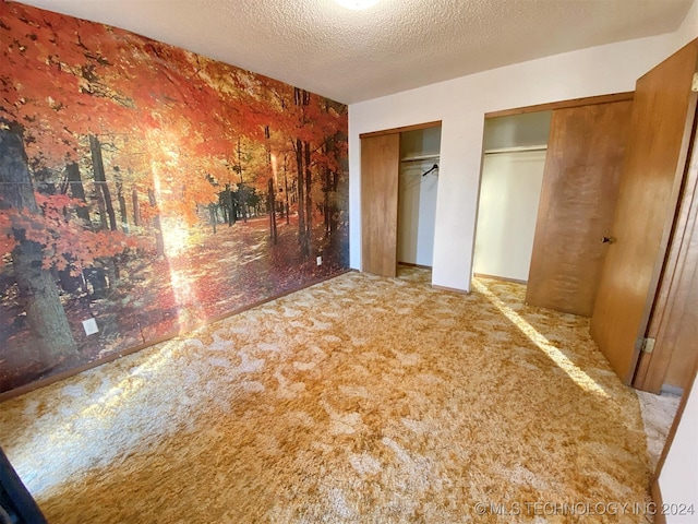 unfurnished bedroom with two closets, light carpet, and a textured ceiling