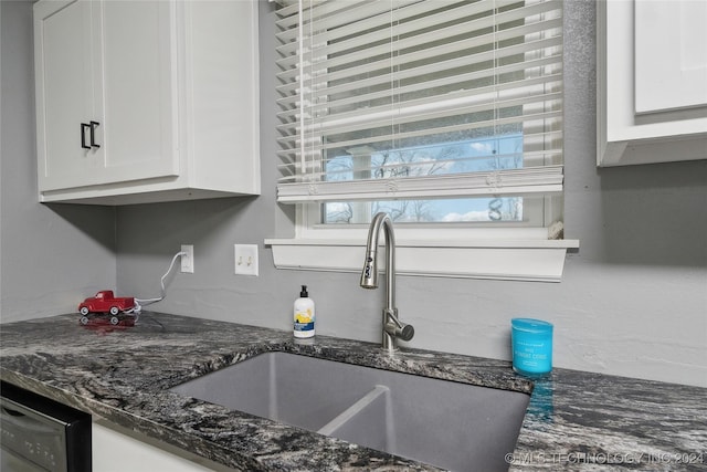 kitchen featuring black dishwasher, sink, white cabinets, and dark stone counters