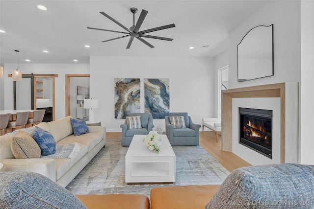 living room featuring ceiling fan, a fireplace, a barn door, and light hardwood / wood-style floors