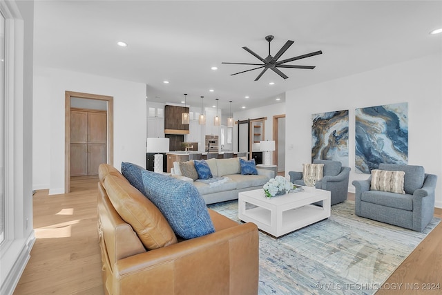 living room featuring ceiling fan, a barn door, and light wood-type flooring