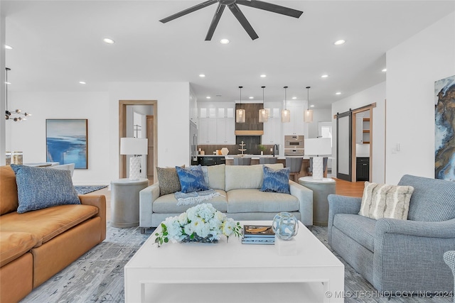 living room with a barn door, sink, ceiling fan, and light hardwood / wood-style floors