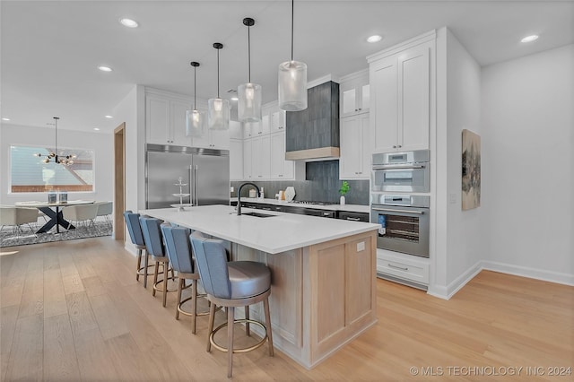 kitchen featuring sink, hanging light fixtures, stainless steel appliances, a kitchen island with sink, and white cabinets