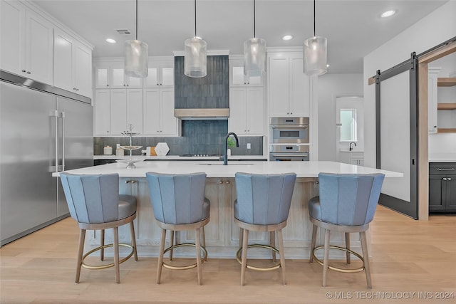 kitchen featuring sink, stainless steel appliances, a barn door, and a center island with sink