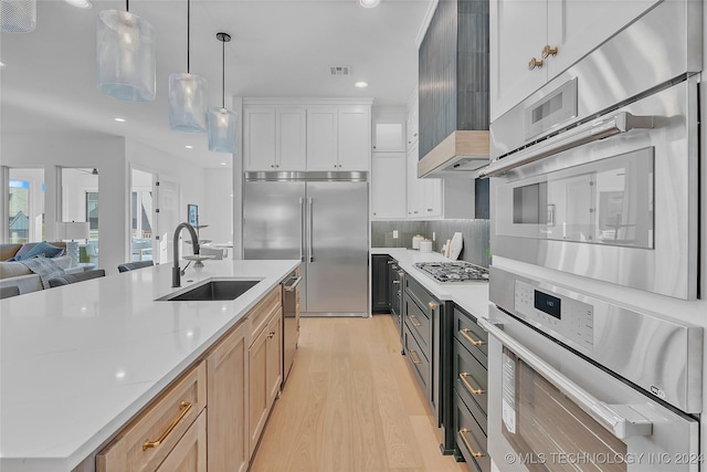 kitchen featuring sink, appliances with stainless steel finishes, custom range hood, pendant lighting, and white cabinets