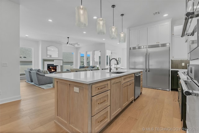 kitchen with sink, decorative light fixtures, a center island with sink, light brown cabinets, and stainless steel appliances