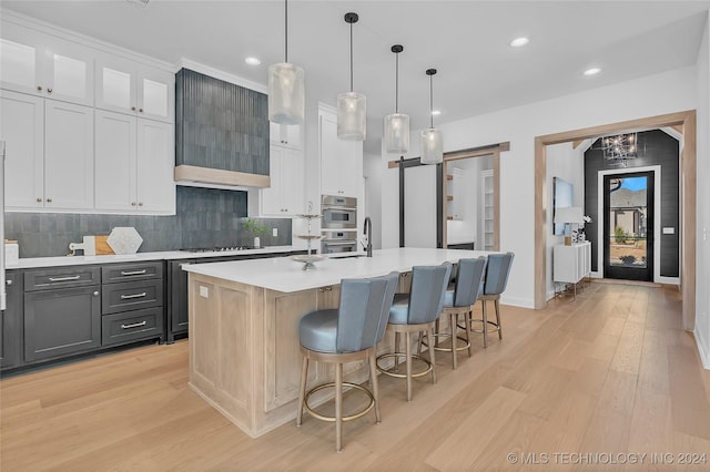 kitchen with decorative light fixtures, an island with sink, a barn door, and white cabinets