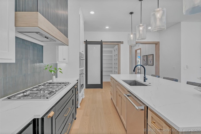 kitchen featuring pendant lighting, sink, custom exhaust hood, stainless steel appliances, and a barn door