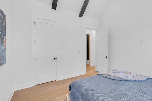 bedroom featuring light hardwood / wood-style flooring and vaulted ceiling with beams