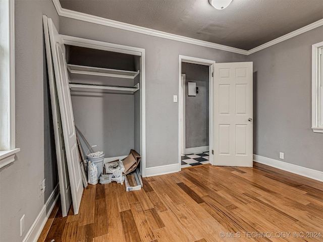 unfurnished bedroom featuring a textured ceiling, ornamental molding, a closet, and wood-type flooring