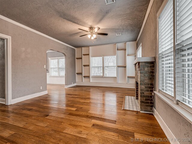 unfurnished living room featuring built in shelves, ceiling fan, crown molding, wood-type flooring, and a textured ceiling