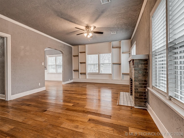 unfurnished living room with hardwood / wood-style flooring, a brick fireplace, ornamental molding, ceiling fan, and a textured ceiling