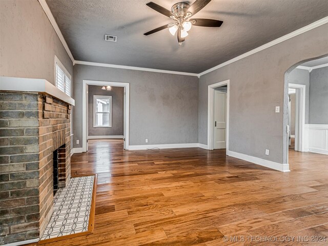 unfurnished living room featuring ceiling fan, a brick fireplace, crown molding, a textured ceiling, and hardwood / wood-style flooring