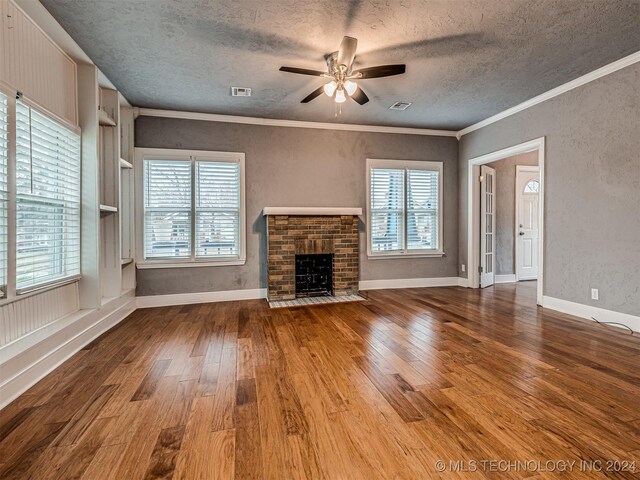 unfurnished living room featuring a brick fireplace, ceiling fan, a healthy amount of sunlight, crown molding, and hardwood / wood-style flooring