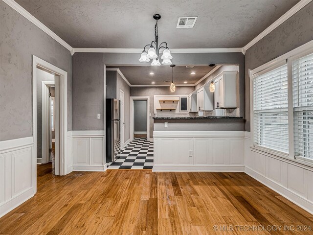 kitchen featuring hanging light fixtures, kitchen peninsula, stainless steel fridge, crown molding, and white cabinets