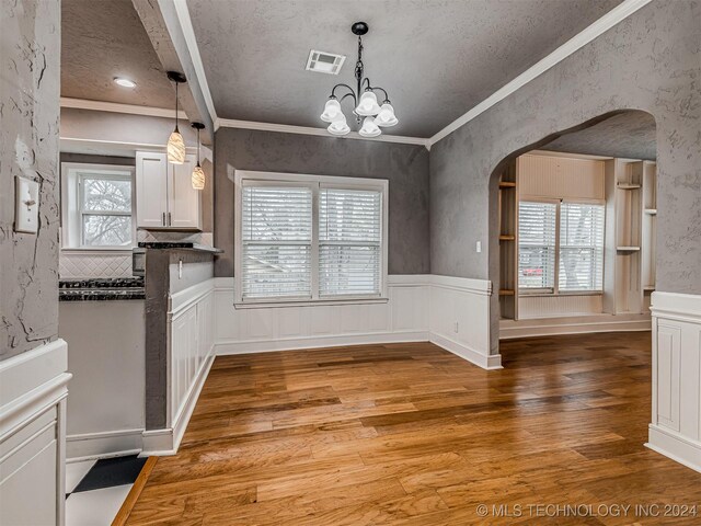 unfurnished dining area featuring hardwood / wood-style flooring, a textured ceiling, crown molding, and a chandelier