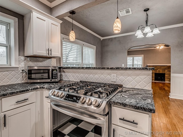 kitchen with crown molding, white cabinets, stainless steel gas range oven, and hanging light fixtures