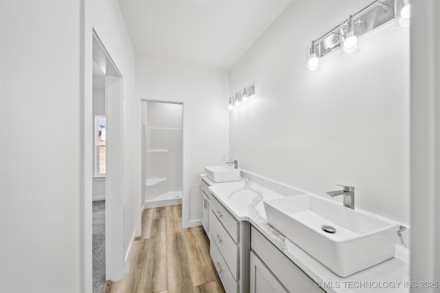 bathroom with double vanity, wood finished floors, a shower, and a sink