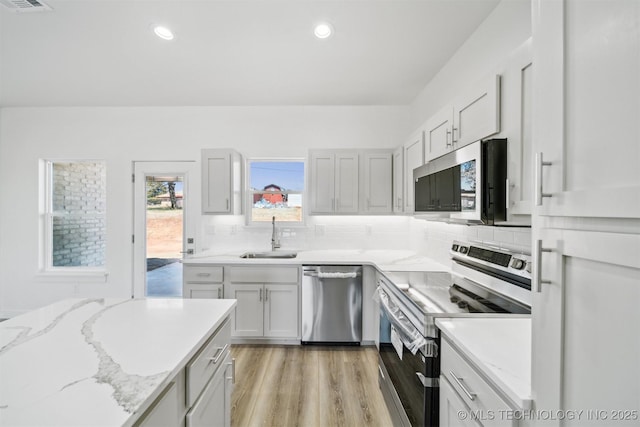 kitchen with a sink, stainless steel appliances, light wood-style floors, and decorative backsplash