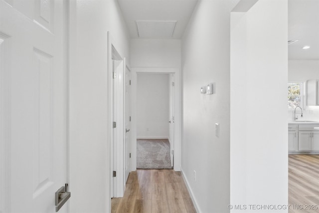 hall with a sink, baseboards, attic access, and light wood finished floors