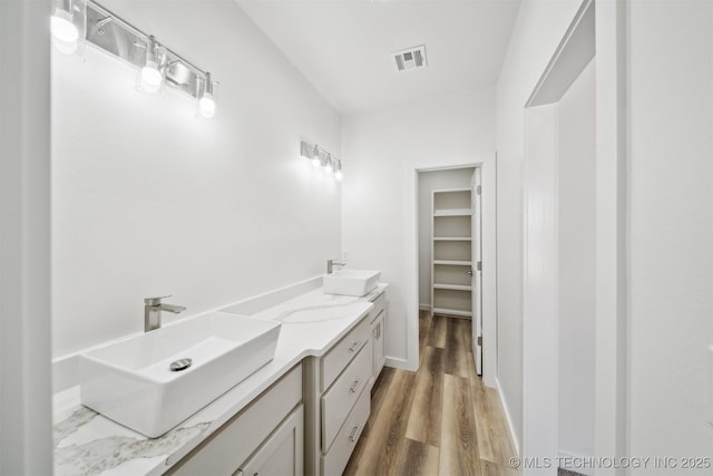 full bath with visible vents, wood finished floors, a walk in closet, and a sink