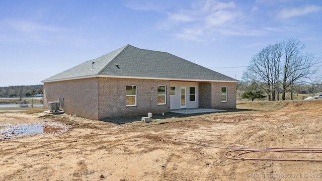 rear view of property featuring cooling unit, a patio area, brick siding, and roof with shingles