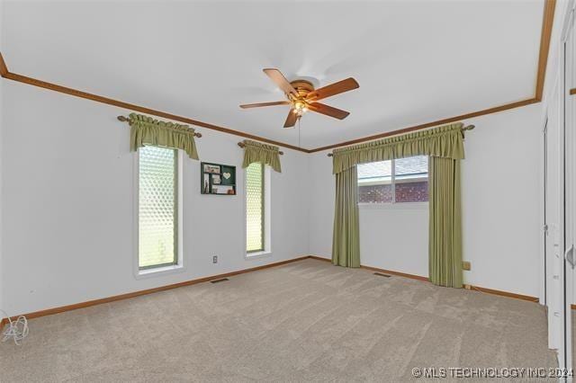 spare room with ceiling fan, a wealth of natural light, ornamental molding, and light carpet