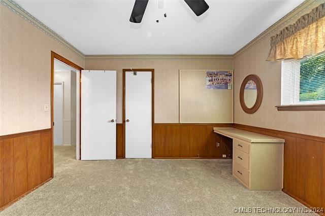 unfurnished bedroom featuring ceiling fan, wood walls, and light carpet