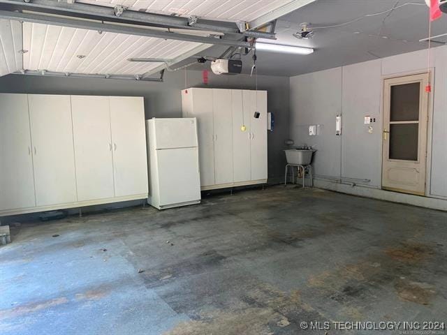 garage with sink, white refrigerator, and a garage door opener